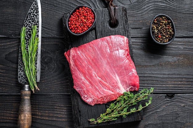 Fianco crudo o bistecca di carne di manzo bavette su un tagliere di legno. Sfondo nero. Vista dall'alto.