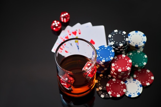 Fiches del casinò giocando a carte bicchiere di whisky e dadi su sfondo riflettente scuro dark