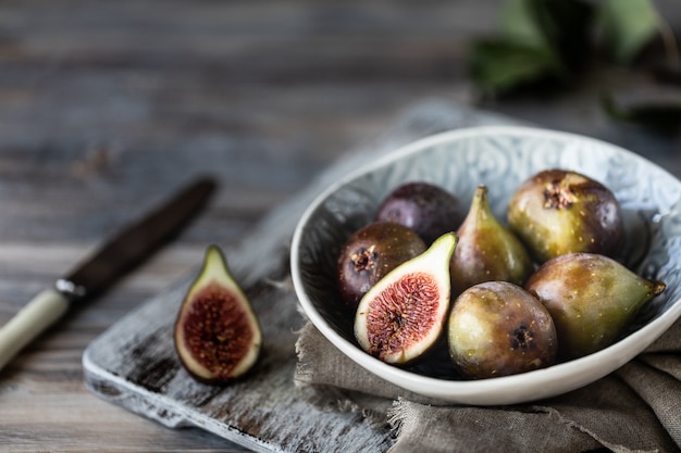 Fichi maturi freschi in una ciotola su una tavola di legno scura.