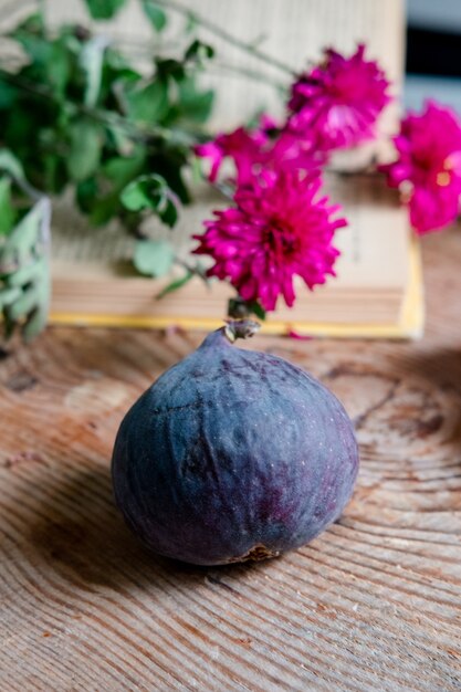 Fichi su uno sfondo di fiori di libro rosso, su un tavolo di legno. cornice verticale. Estetica con fichi, fiori e un libro. Bella frutta su un tavolo di legno. Mattina colazione francese.