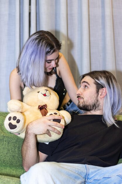 Fidanzata che dà un orsacchiotto al ragazzo seduto sul divano Giovane donna che dà orsacchiotto al ragazzo seduto sul divano