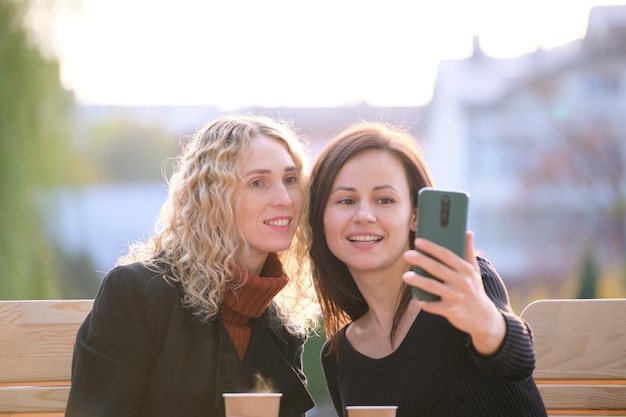 Fidanzate allegre che prendono selfie con il telefono che riposa al bar della strada della città Amici di sesso femminile che si godono il tempo insieme all'aperto in una calda giornata