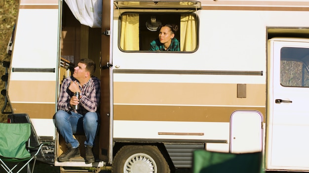 Fidanzato seduto sulle scale del camper. Fidanzata ammirando il paesaggio selvaggio dal finestrino del camper. Tenda da campeggio.