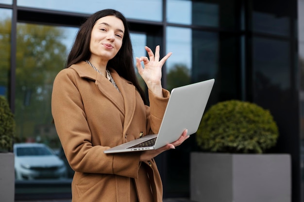 Fiduciosa bella donna d'affari che mostra gesto ok utilizzando il computer portatile Concetto di business di successo