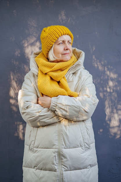 Fiduciosa donna anziana in cappotto caldo con elegante sciarpa lavorata a maglia e cappello incrociando le braccia