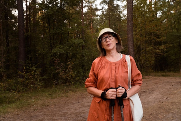 Fiduciosa donna asiatica in cappello e occhiali a piedi nella foresta