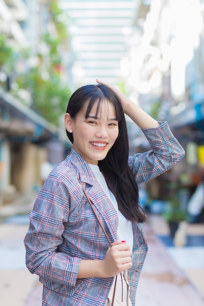 Fiduciosa donna d'affari asiatica professionale che indossa un blazer a righe marroni mentre si reca al lavoro.