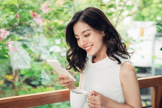 Fiduciosa giovane donna asiatica in abbigliamento casual intelligente utilizzando smartphone, digitando sul telefono.