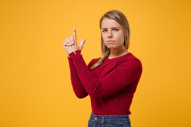 Fiduciosa giovane donna bionda ragazza in abiti casual in posa isolato su sfondo giallo arancione ritratto in studio. Concetto di stile di vita di emozioni sincere della gente. Simula lo spazio della copia. Tenersi per mano come una pistola.