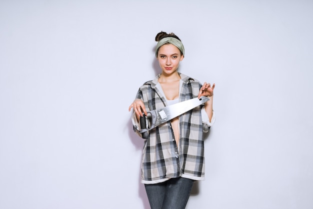 Fiduciosa ragazza in una camicia a quadri con in mano una sega affilata, riparazione nell'appartamento