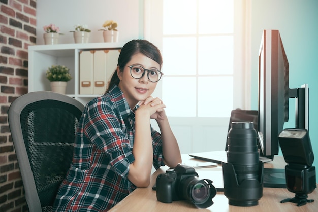 fiducioso fotografo d'affari di successo diritti della donna seduta sulla scrivania di editing guardando la fotocamera sorridente pronto lavoro ritocco foto.