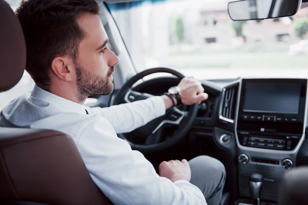 Fiducioso giovane imprenditore seduto al volante della sua nuova auto