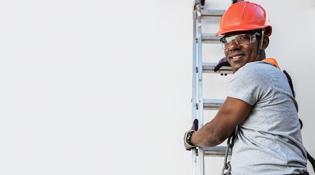 Fiducioso giovane maschio latino carpentiere in hardhat tenendo il trapano e guardando la telecamera con un sorriso