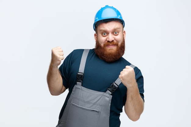 Fiducioso giovane operaio edile maschio che indossa casco di sicurezza e uniforme guardando la fotocamera che mostra sì gesto isolato su sfondo bianco