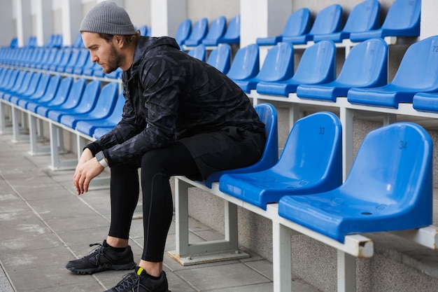 Fiducioso giovane sportivo seduto sui sedili della tribuna allo stadio