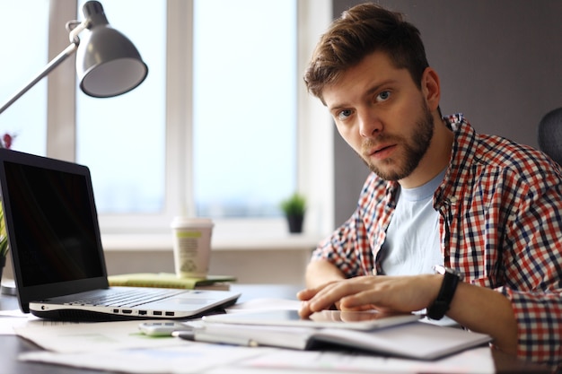 Fiducioso giovane uomo che lavora al computer portatile mentre era seduto al suo posto di lavoro in ufficio