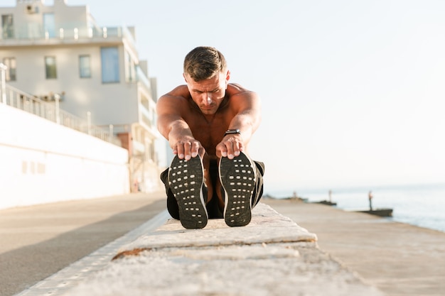 Fiducioso sportivo senza camicia facendo esercizi di stretching