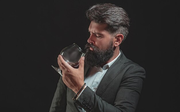 Fiducioso uomo barbuto in abito nero con bicchiere di whisky in loft fiducioso uomo ben vestito con glas