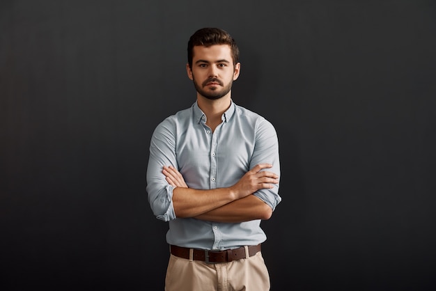 Fiducioso uomo d'affari bello e giovane con la barba che guarda la telecamera e tiene le braccia incrociate