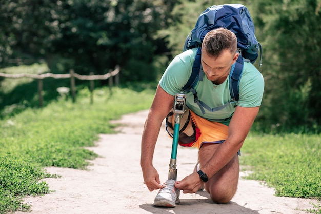 Fiducioso uomo piacevole con paralisi che si allaccia le scarpe mentre fa una passeggiata all'aperto