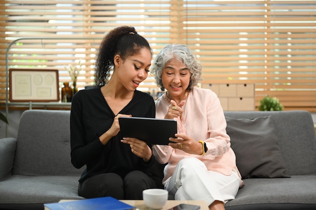 Figlia adulta che insegna a una madre anziana interessata come usare un tablet o mostra un'applicazione Il concetto di tecnologia per anziani