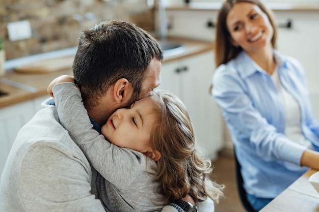 Figlia amorevole che abbraccia suo padre a casa La madre è seduta sullo sfondo