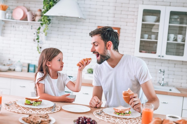 Figlia che nutre padre con croissant in cucina