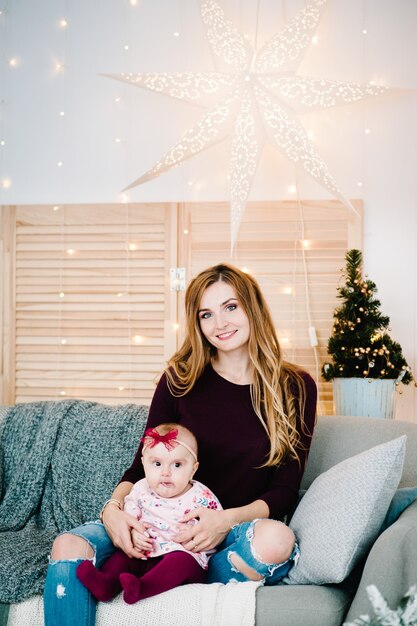 Figlia della neonata con la mamma sul divano vicino all'albero di Natale Buon Natale