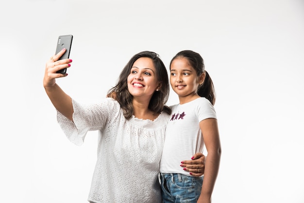 Figlia di madre asiatica indiana che scatta foto di selfie con lo smartphone, isolato su sfondo bianco