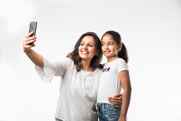 Figlia di madre asiatica indiana che scatta foto di selfie con lo smartphone, isolato su sfondo bianco