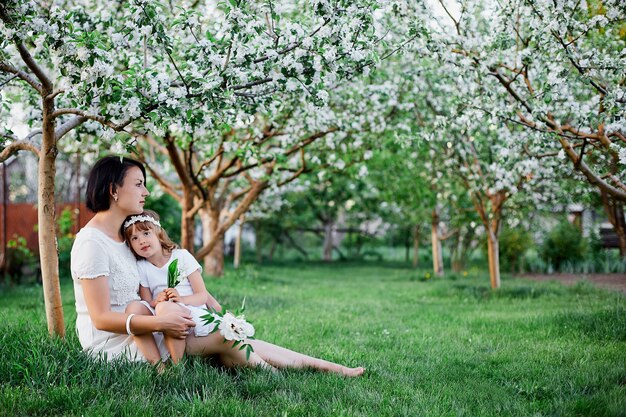 Figlia e madre sveglie che si siedono e che abbracciano nel giardino di primavera del fiore