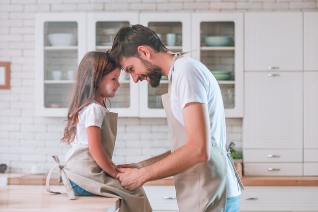 Figlia seduta sul tavolo e papà in piedi sulla cucina e guardandosi vista laterale