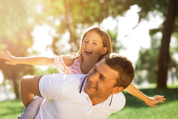 Figlia sulle spalle in sella a suo padre sorridente nel parco