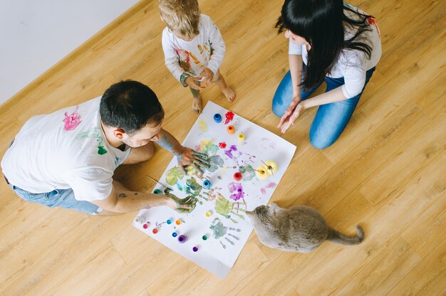 figlio di famiglia felice con i genitori e un gatto dipinto un poster e l&#39;un l&#39;altro con le vernici