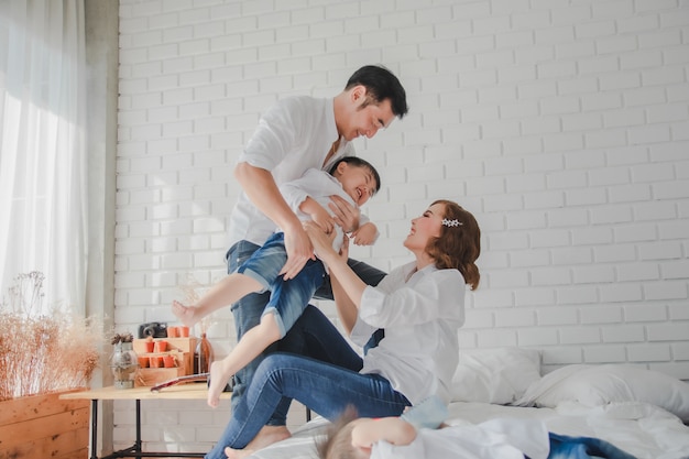 Figlio di trasporto della camicia bianca della madre del padre giapponese asiatico della madre che porta bambino sulla camera da letto nella stanza bianca.