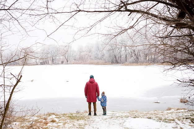 Figlio e padre camminano in riva al lago in inverno Ci sono molti alberi intorno