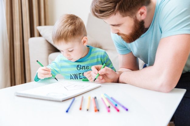 Figlio e papà seduti e disegnano insieme sul tavolo