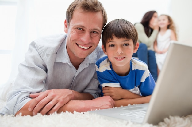 Figlio e papà sorridenti che per mezzo del computer portatile sul tappeto