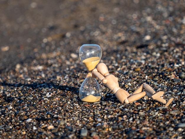 Figura del bastone di legno accanto alla clessidra sulla spiaggia in riva al mare