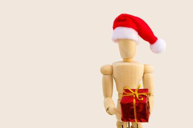 Figura in legno - manichino artistico con cappello da Babbo Natale rosso con confezione regalo. Concetto di business e design per Natale. Messa a fuoco selettiva