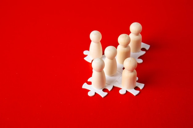 Figure in legno su puzzle su sfondo rosso come simbolo del team building