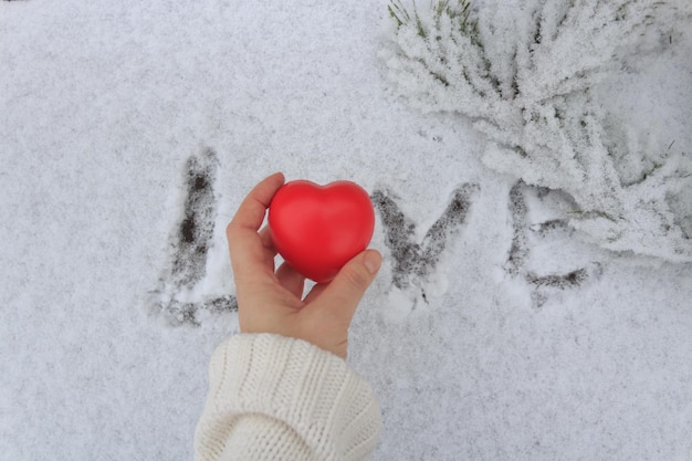 Figurina a forma di cuore sul palmo della donna sullo sfondo della parola Amore disegnata sulla neve