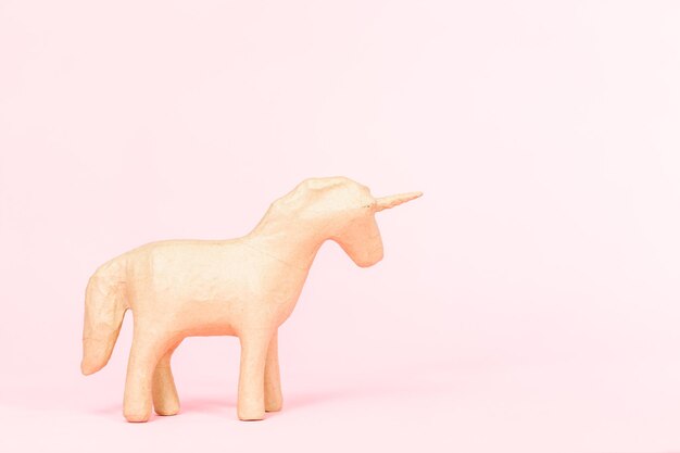 Figurina di unicorno in cartapesta non finita su sfondo rosa.