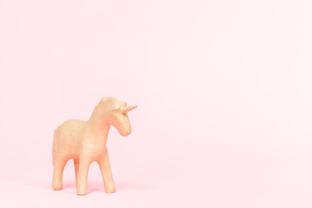 Figurina di unicorno in cartapesta non finita su sfondo rosa.