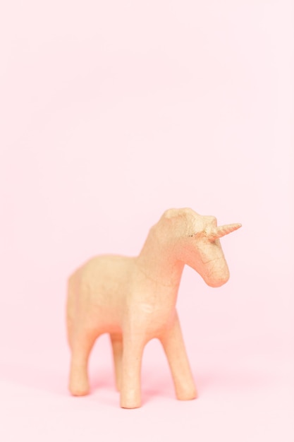 Figurina di unicorno in cartapesta non finita su sfondo rosa.