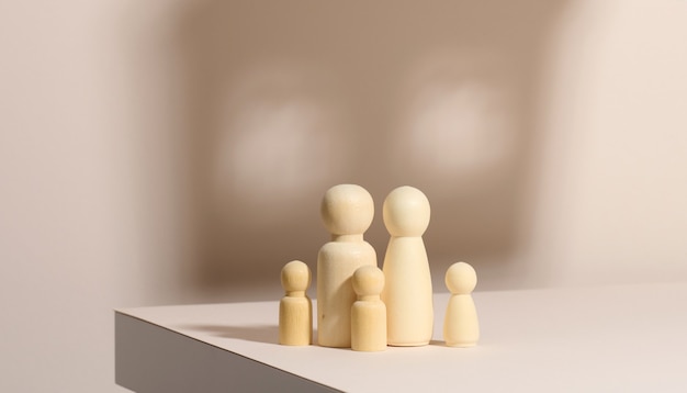 Figurine di legno di una famiglia su uno sfondo d'ombra a forma di casa. Sfondo beige. Sogni di casa, mutuo