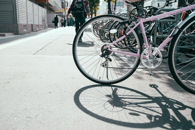 Fila di biciclette in stile giapponese classico con posti a sedere al parcheggio sul marciapiede a tokyo in Giappone. bici da donna rosa sotto il sole con una grande ombra di pneumatici su strada nel caldo clima estivo. le persone fanno il pendolare stile di vita in città.