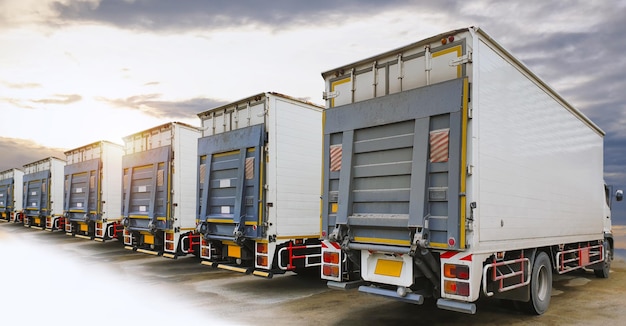 Fila di camion portacontainer con rampa di sollevamento parcheggiato presso la logistica dei camion merci Sunset Sky