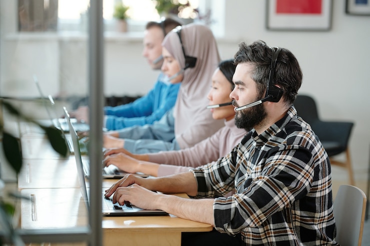 Foto fila di operatori di call center multietnici occupati in cuffia con microfono che lavorano con le applicazioni dei clienti