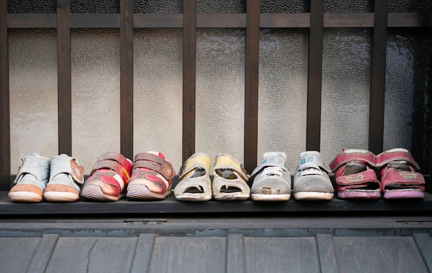 Fila di vecchi sandali usati per bambini, pantofole, scarpe da ginnastica sul pavimento.